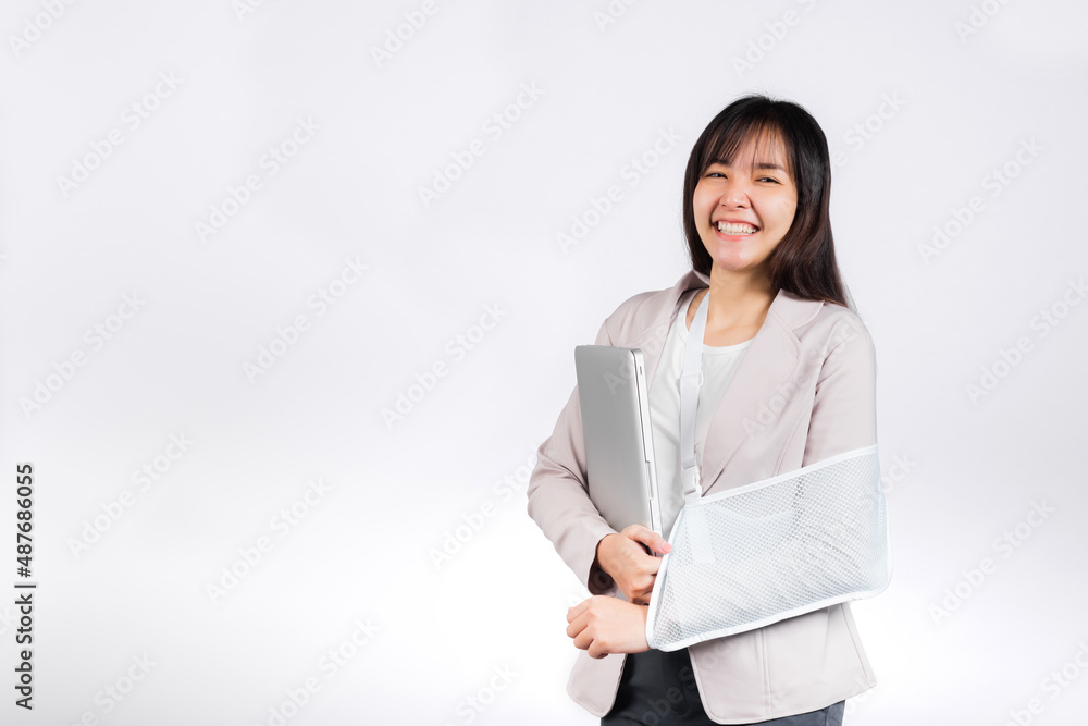 Asian business woman confident smiling broken arm after accident and wear arm splint for treatment but still have to work she hold laptop computer studio isolated on white background,copy space Asian business woman confident smiling broken arm after accident and wear arm splint for treatment but still have to work she hold laptop computer studio isolated on white background,copy space