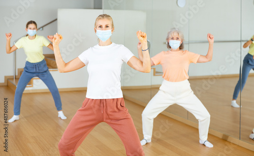 Woman in face mask doing squats with her family on group fitness training in studio.