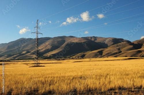 A metal pole of a power line on the edge of the autumn steppe at the foot of a high mountain range.