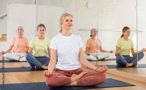Woman sitting in lotus pose while training yoga with her daughter and senior mother.