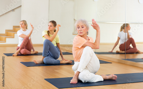 Portrait of active woman practicing yoga in group, making twisting asana