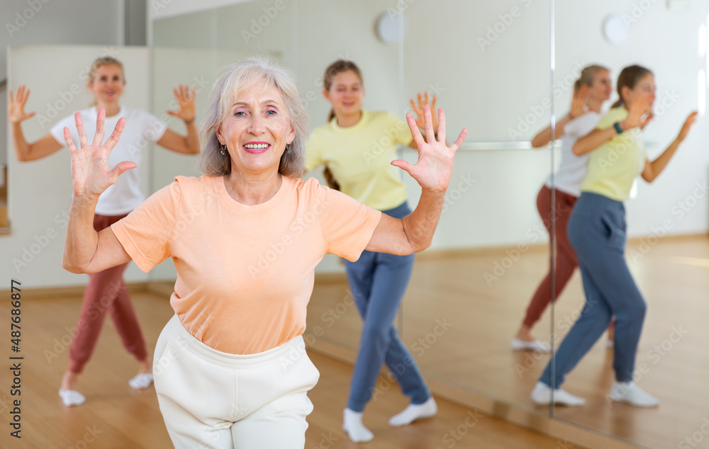 Positive mature woman doing aerobics exercises with group of people in dance center