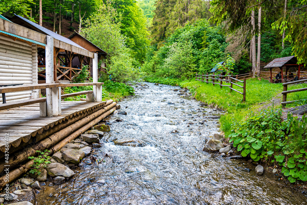 Scenic view of small stream flowing through stones next to hut in green forest, Shed beside creek surrounded by green trees Scenic view of small stream flowing through stones next to hut in green forest, Shed beside creek surrounded by green trees