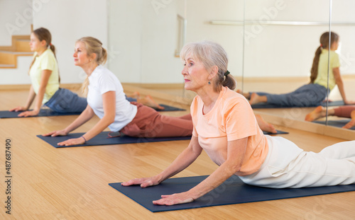Elderly woman pensioner doing stretching workout during group training in yoga class