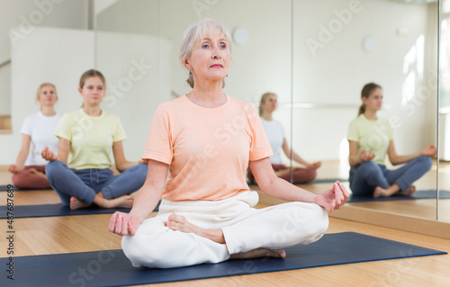 Closeup of positive elderly woman practice yoga lotus pose to meditation in modern studio