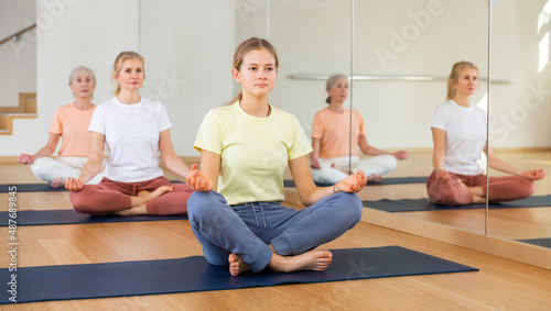 Sporty young girl making yoga meditation in lotus pose in fitness center