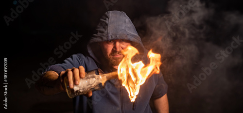The man in the hood is holding a burning bottle. Molotov cocktail.