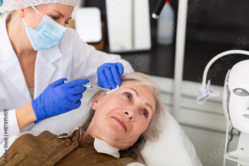 Closeup portrait of aged woman getting injections for face skin tightening at aesthetic cosmetology clinic ..