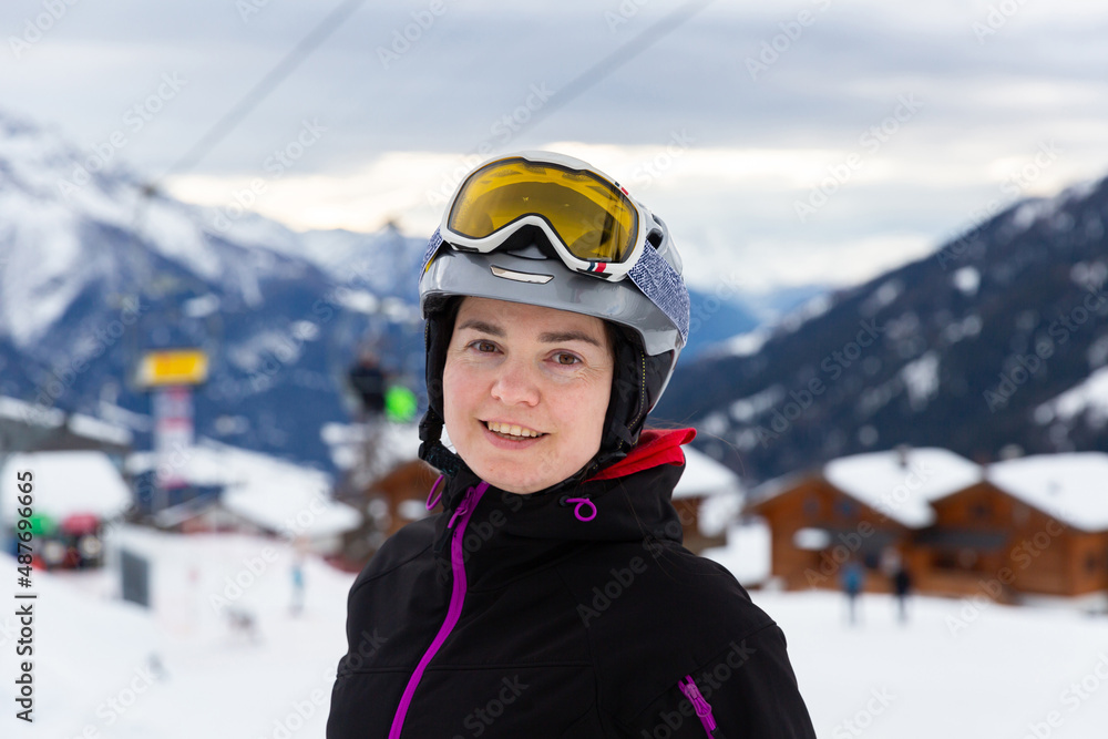 Smiling female skier wearing helmet and goggles standing on slope of ski resort on winter day 