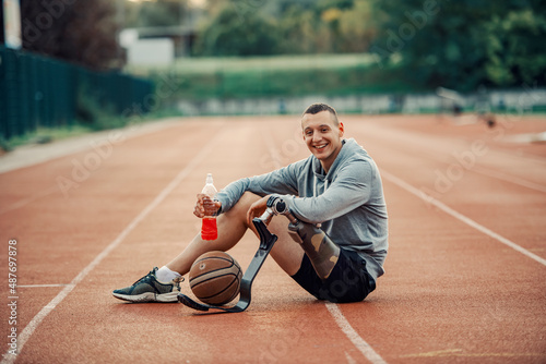 A handicapped basketball player with artificial leg sitting at stadium, drinking refreshment and taking a break.