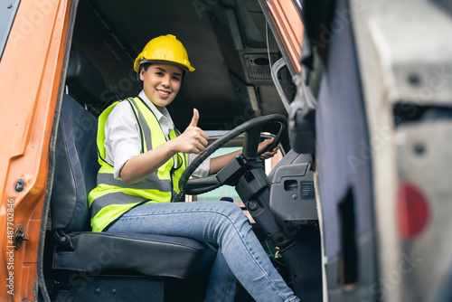 Asian woman truck driver sitting in truck cabin looking at camera.