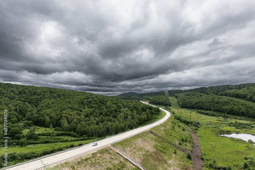 Gloomy sky with heavy clouds. Landscape with a road going into the distance outside the city. The car is driving on the highway.