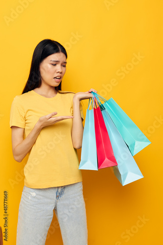 woman with Asian appearance in a yellow T-shirt with multicolored shopping bags isolated background unaltered