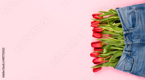 A bouquet of red tulips peeks out of pants or shorts on a pink background. The concept of a healthy diet, a beautiful body, youth, weight loss or losing weight. photo