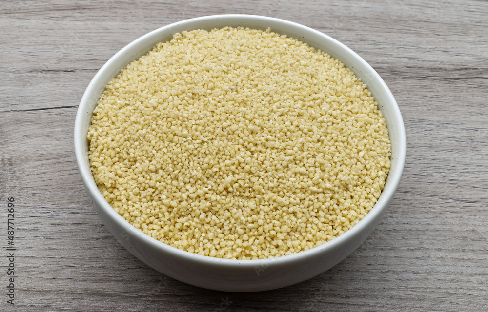 Bowl of raw Couscous isolated on wooden background. Top view. Bowl of raw Couscous isolated on wooden background. Top view.