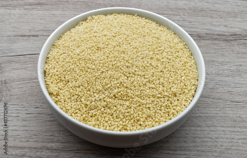Bowl of raw Couscous isolated on wooden background. Top view.