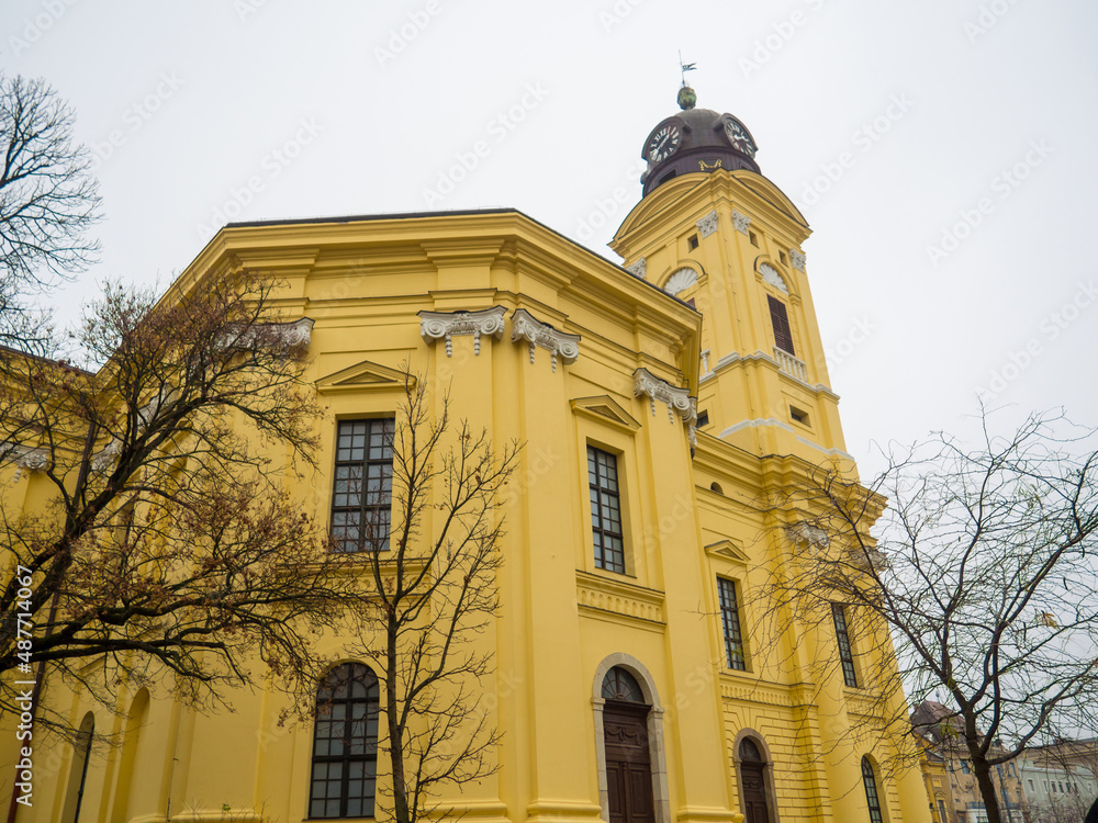 Fototapeta premium Protestant Great Church, Hungarian: Reformatus Nagytemplom, on the Kossuth square in Debrecen, Hungury. Close up of yellow buildings with two towers, clocks, columns and windows on the sky background