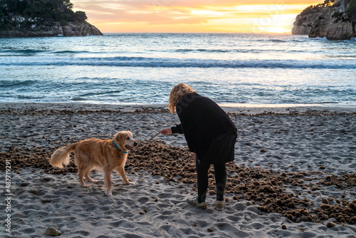 Curly-haired blonde woman playing at sunset on the beach with a Golden Retriever dog. Cala Galdana, Minorca, Spain photo