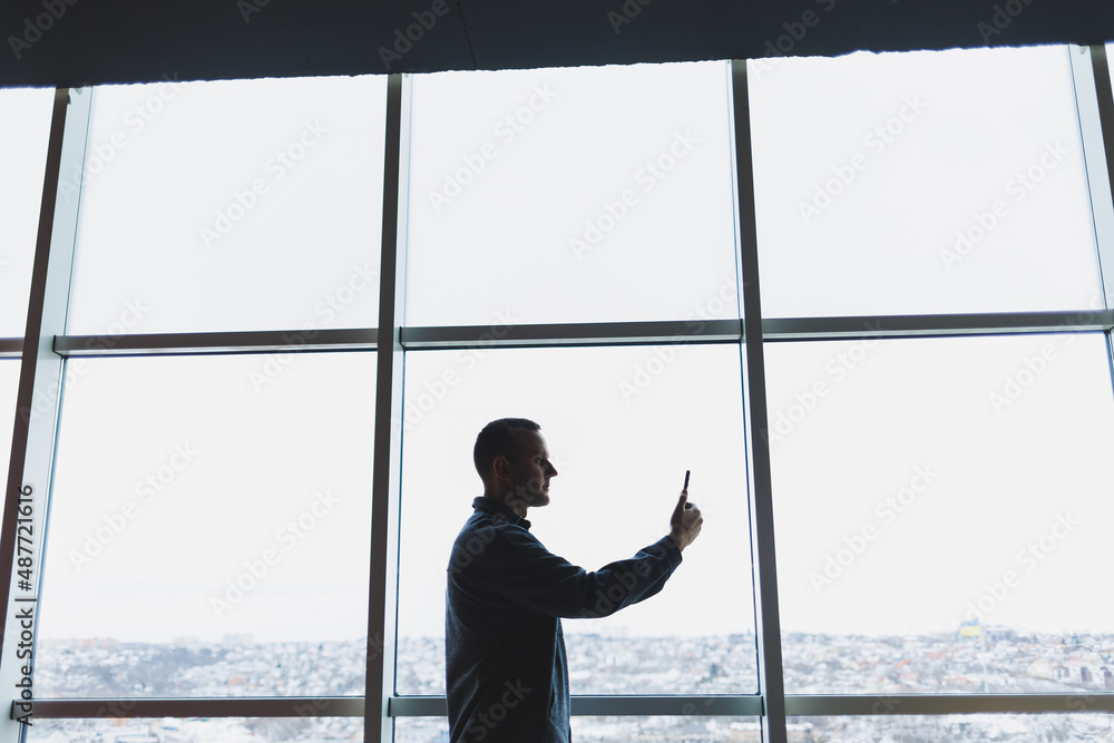 Young business man holding a phone. In an office or business center against the background of large windows of a skyscraper. Work and career, concept Young business man holding a phone. In an office or business center against the background of large windows of a skyscraper. Work and career, concept