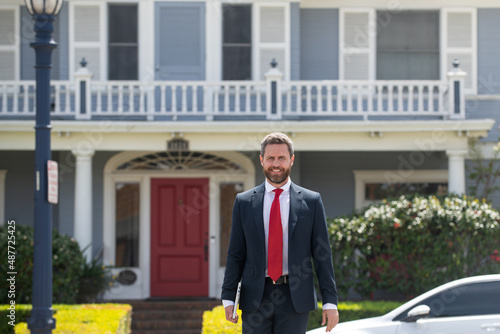 Busines sman standing outside a modern house. Real estate concept. Agent ready to sell home.