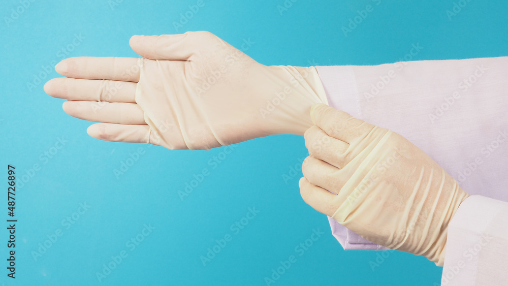 Side view. The doctor's hand is pulling white latex gloves isolated on blue background.