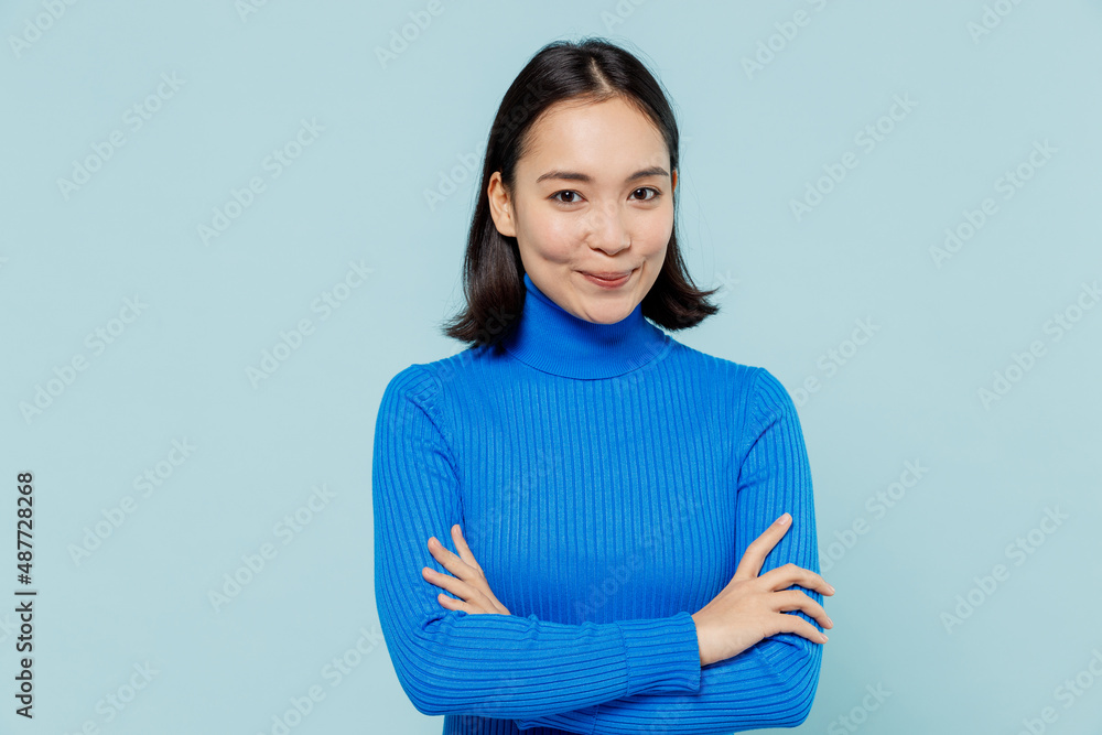 Fancy young woman of Asian ethnicity 20s years old wears blue shirt hold hands crossed looking camera isolated on plain pastel light blue background studio portrait. People emotions lifestyle concept. Fancy young woman of Asian ethnicity 20s years old wears blue shirt hold hands crossed looking camera isolated on plain pastel light blue background studio portrait. People emotions lifestyle concept.