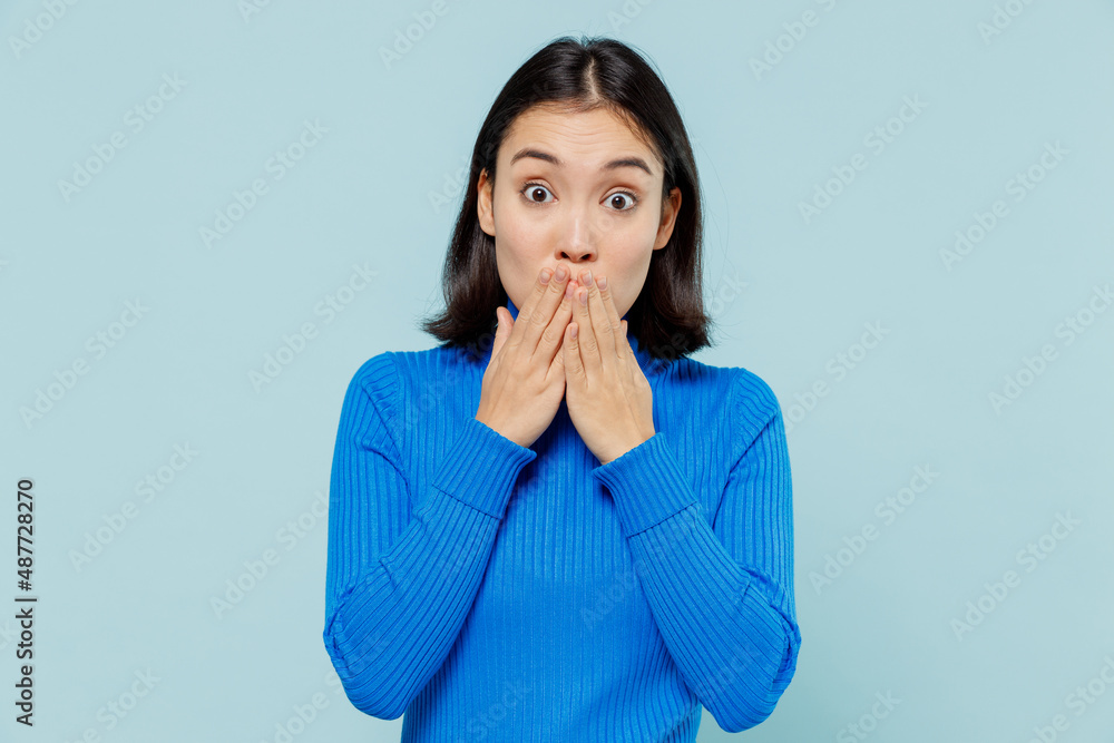 Shocked surprised young woman of Asian ethnicity 20s years old wears blue shirt cover mouth with hand isolated on plain pastel light blue background studio portrait. People emotions lifestyle concept. Shocked surprised young woman of Asian ethnicity 20s years old wears blue shirt cover mouth with hand isolated on plain pastel light blue background studio portrait. People emotions lifestyle concept.