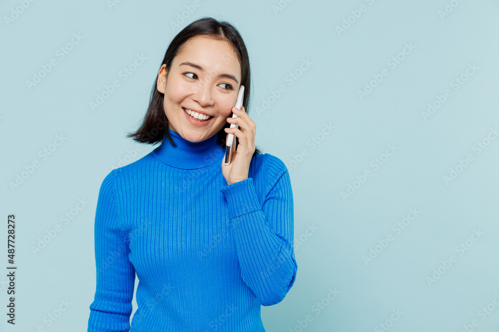 Fun young woman of Asian ethnicity 20s years old wears blue shirt hold in hand talk on mobile cell phone conducting pleasant conversation isolated on plain pastel light blue background studio portrait Fun young woman of Asian ethnicity 20s years old wears blue shirt hold in hand talk on mobile cell phone conducting pleasant conversation isolated on plain pastel light blue background studio portrait