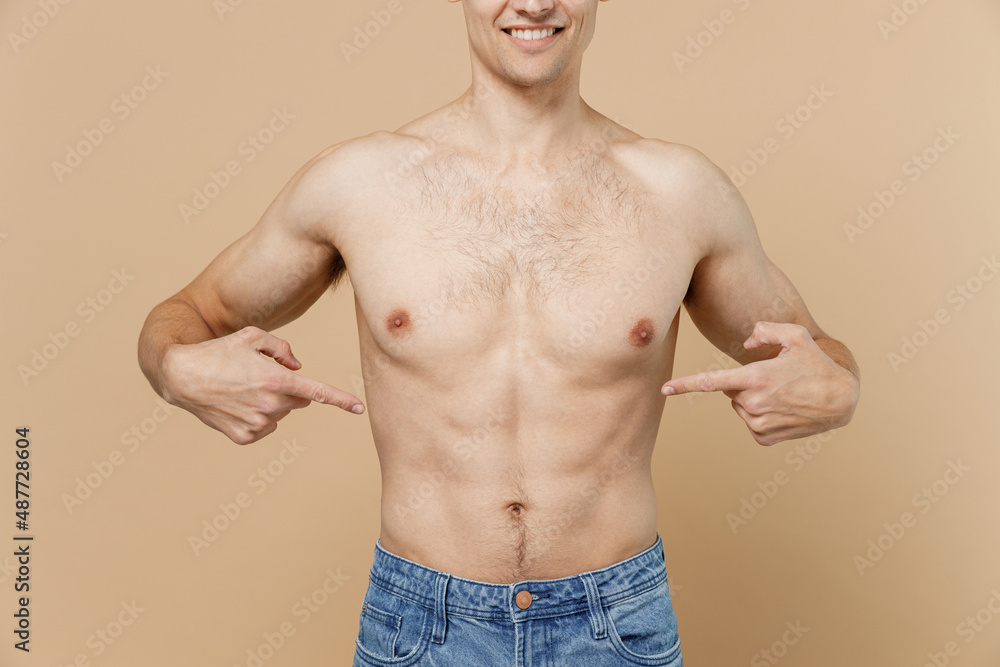 Young european man 20s in jeans pants with point index finger on naked torso isolated on pastel pastel beige color background studio Body care healthcare fitness sport bodybuilding lifestyle concept