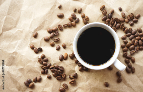 Flat lay view of black coffee cup on crumple brown paper with coffee beans