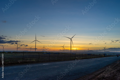 Wind turbine farm and agricultural fields on a summer day. Wind electricity generator in sunset sky, power plant, wind efficiency.