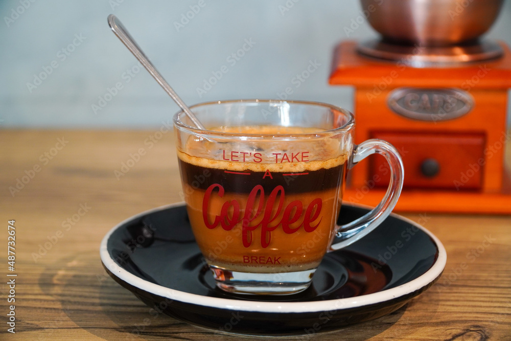 Close up photo of milk coffee served in a clear cup and coffee grinder background Close up photo of milk coffee served in a clear cup and coffee grinder background
