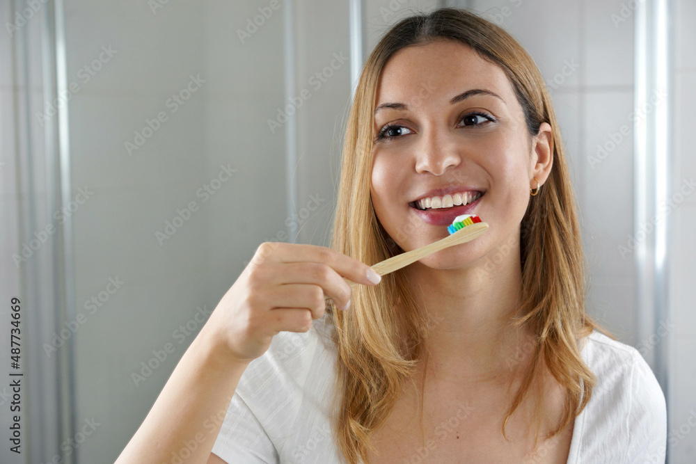Young woman with wooden bamboo tooth brush in the bathroom looking herself in the mirror. Dental care, eco-friendly bamboo toothbrush, zero waste way of life. Young woman with wooden bamboo tooth brush in the bathroom looking herself in the mirror. Dental care, eco-friendly bamboo toothbrush, zero waste way of life.