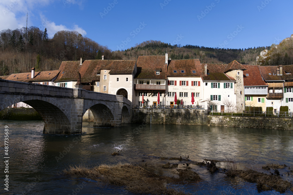 Chalk stone bridge over the river Doubs at little medieval town St-Ursanne, Canton Jura, on a sunny winter morning. Photo taken February 7th, 2022, Saint-Ursanne, Switzerland.