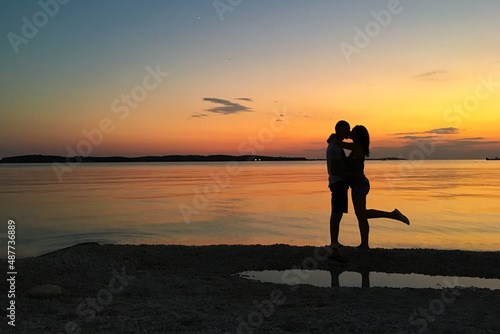 silhouettes of happy people on the beach by the sea at beautiful sunset