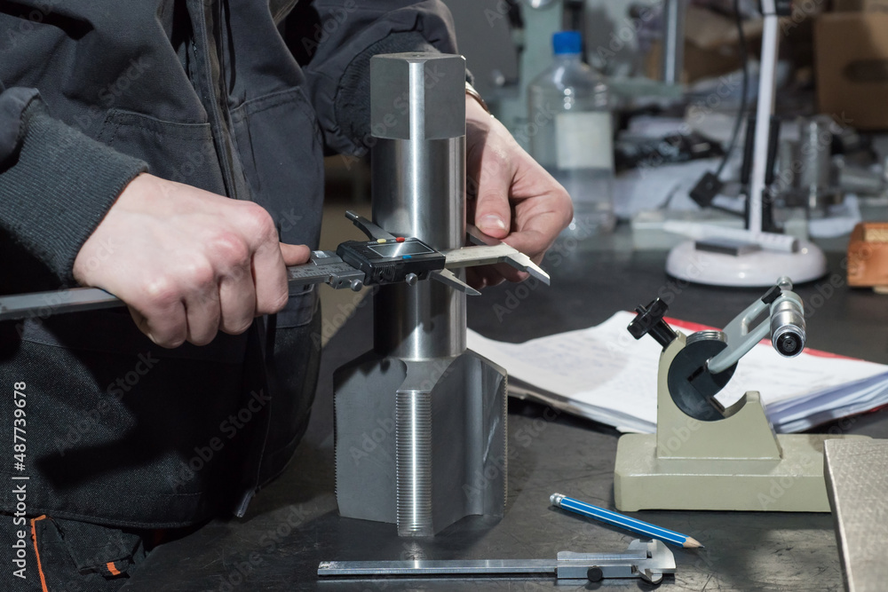 The master measures a metal part with a caliper at the factory