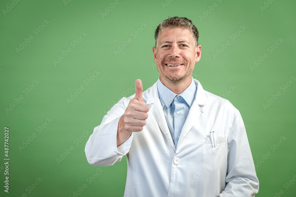 Man with white coat and blue shirt stands in front of green background Man with white coat and blue shirt stands in front of green background