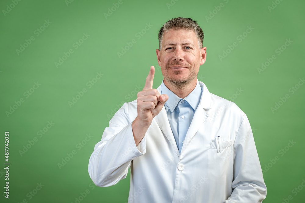 Man with white coat and blue shirt stands in front of green background Man with white coat and blue shirt stands in front of green background