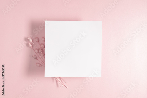 White paper empty blank, dry flowers, dried twig on pink background. Invitation card mockup on beige table. Flat lay, top view, copy space, mockup © prime1001