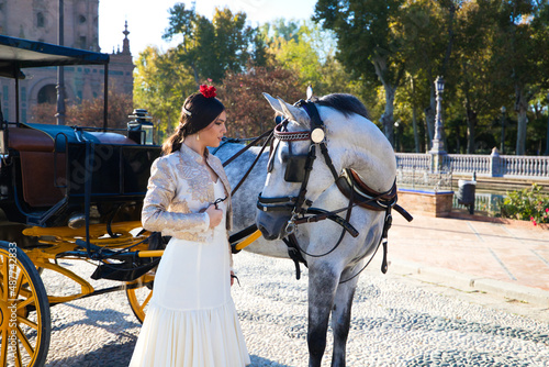 Flamenco dancer woman, brunette and beautiful typical spanish dancer is caressing a white horse in a square in seville. Flamenco concept of cultural heritage of humanity.