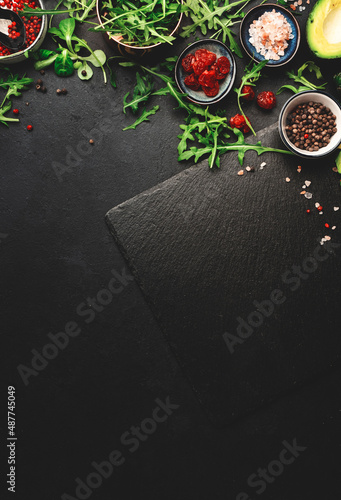 Healthy clean eating food layout and diet nutrition concept. Pineapple, vegetables, dried fruits, greens and other ingredients for salad preparation on black table background with slate board, top 