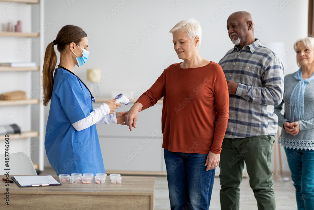 Fototapeta premium Nurse in face mask checking body temperature for senior people