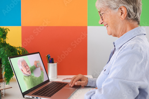 Side view of a smiling mature senior woman chatting in online video using laptop. Caucasian female having virtual video call with happy husband winning lottery ticket. Colorfull background, copy space © luciano