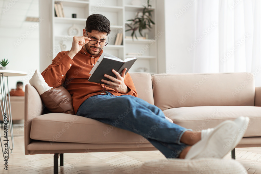 Focused Arab man in glasses trying to read book Focused Arab man in glasses trying to read book