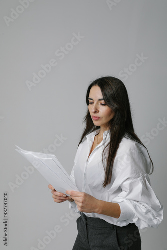 Middle-aged businesswoman, mentor coach stays over white wall holds documents.