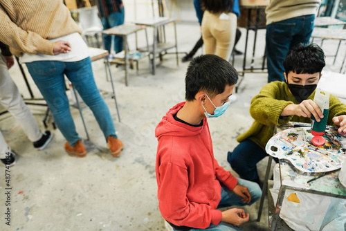 Multiracial students painting inside art room class wearing safety masks - Focus on asian boy