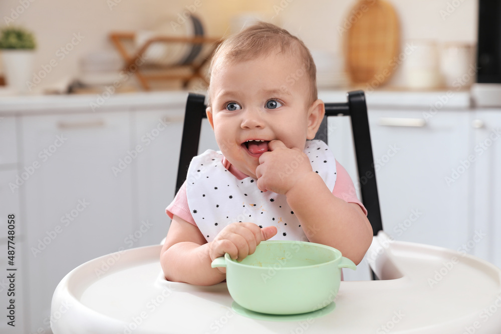 Cute little baby with bowl in high chair at kitchen Cute little baby with bowl in high chair at kitchen