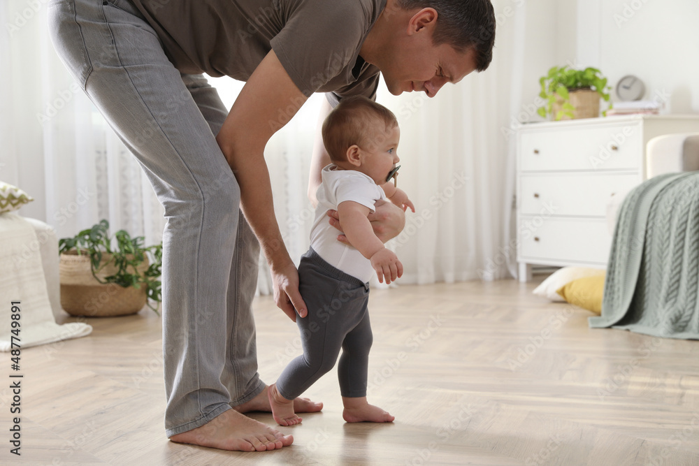 Father supporting his baby daughter while she learning to walk at home Father supporting his baby daughter while she learning to walk at home