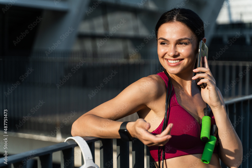 Pleased young sportswoman talking on smartphone outdoors Pleased young sportswoman talking on smartphone outdoors