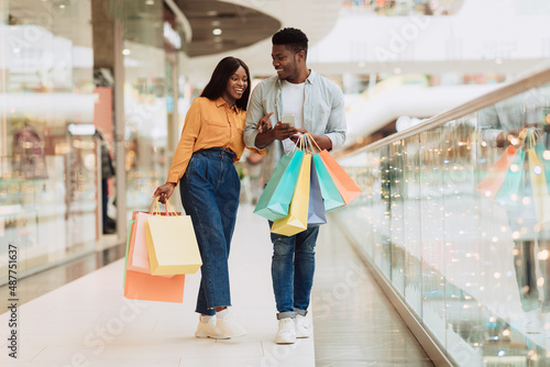 Portrait of happy black couple using phone with shopping bags